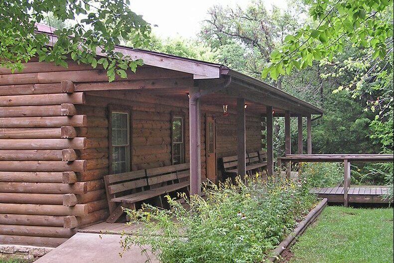 Exterior view of the Chaplin Nature Center visitor center, a log cabin building with a covered porch surrounded by trees and greenery.