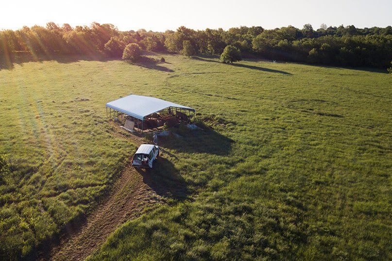 Aerial view of an excavation shelter and vehicle in a wide grassy field during fieldwork.