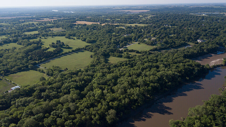 Aerial view of wooded landscape and open fields along a river corridor.