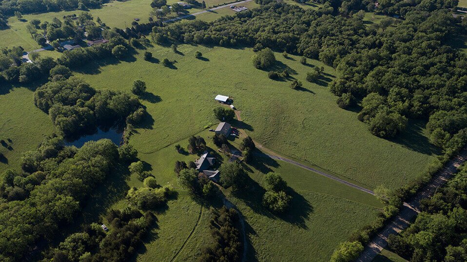 Aerial view of wooded landscape and open fields along a river corridor.