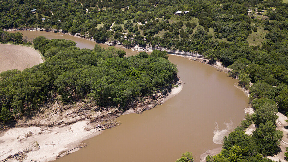 Aerial view of a winding river bordered by dense trees and sandy banks.