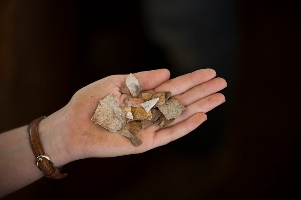Hand holding several small pottery sherds and stone fragments against a dark, out-of-focus background.