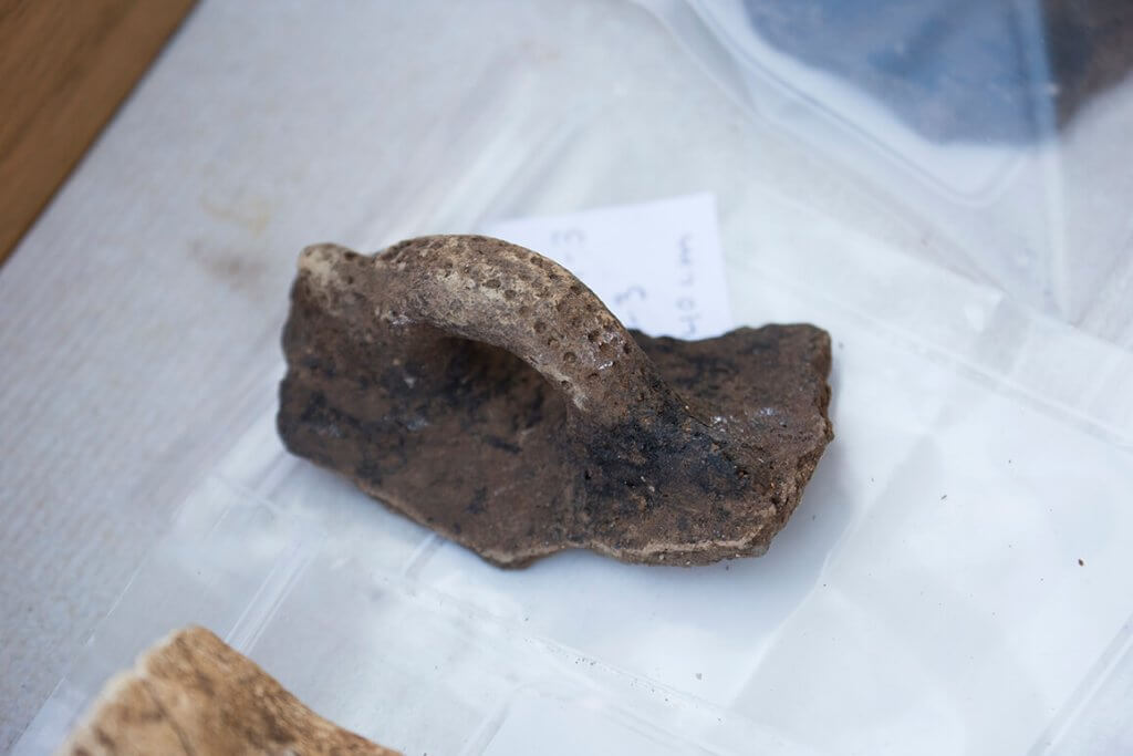 Close-up of a broken ceramic vessel fragment with a loop handle resting on a clear plastic evidence bag.