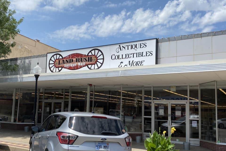 Exterior of Land Rush Antique Mall with storefront windows, a sign reading ‘Antiques, Collectibles & More,’ and parked cars in front.